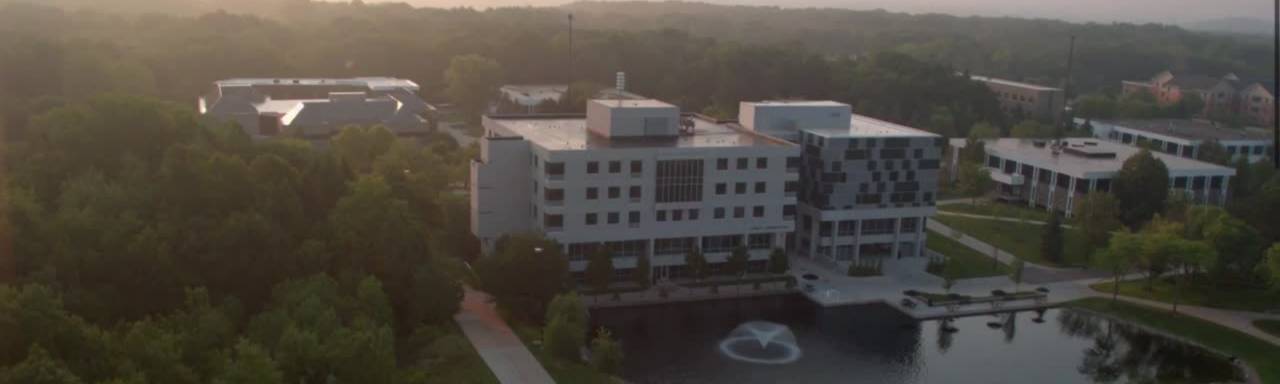 Aerial shot of a grey and blue square building near a small pond. Zumberge Hall on GVSU's Allendale Campus